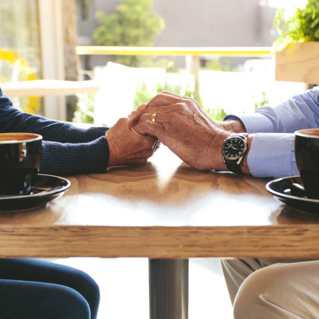 older couple holding hands at coffee table