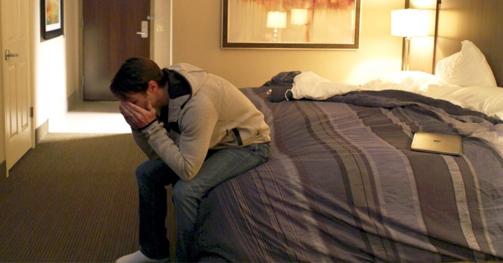 defeated man sitting at end of hotel bed