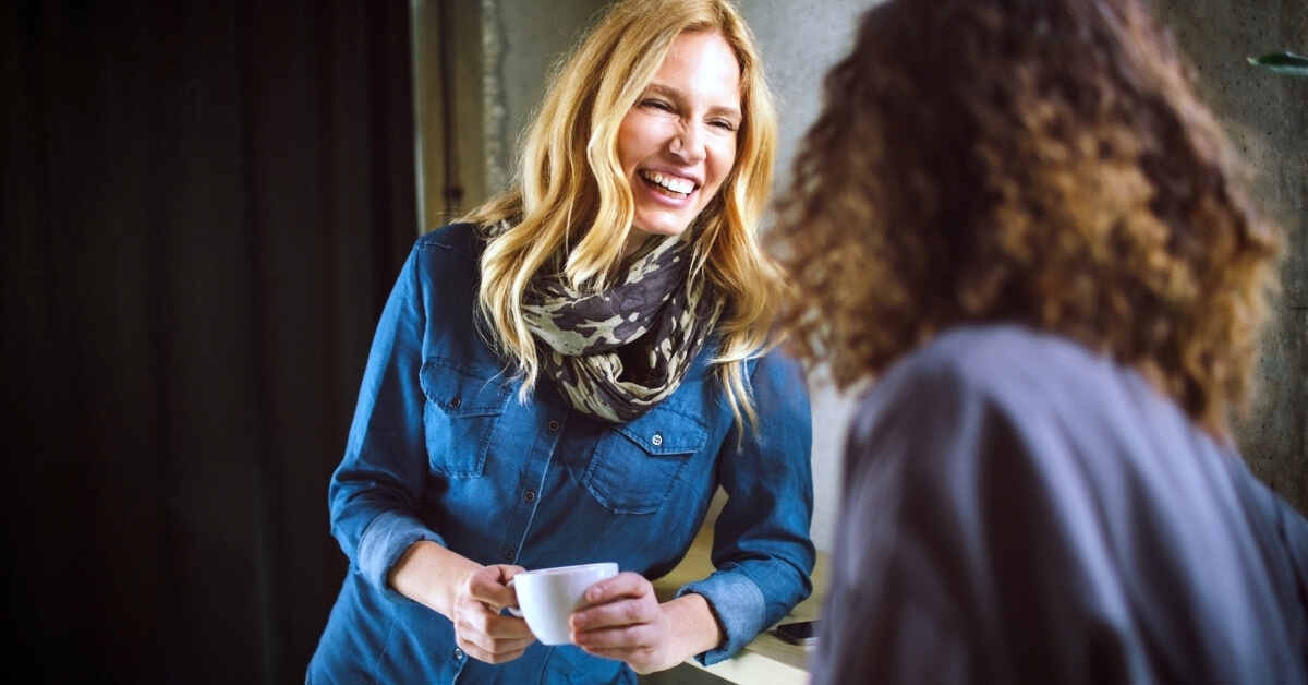 Two joyful women drinking coffee and laughing.