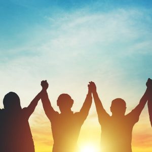 group of people holding upraised hands in front of sunset