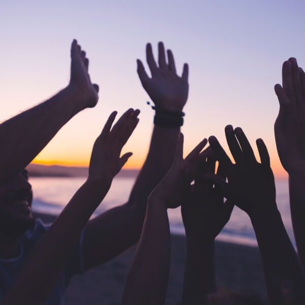 group of people with hands raised at sunset