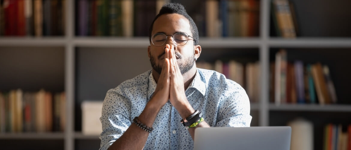 man sitting in front of computer with eyes closed praying