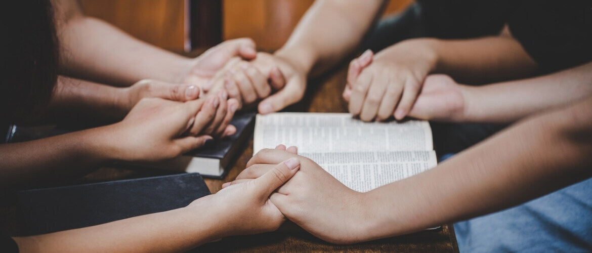 circle of people holding hands around Bibles and praying