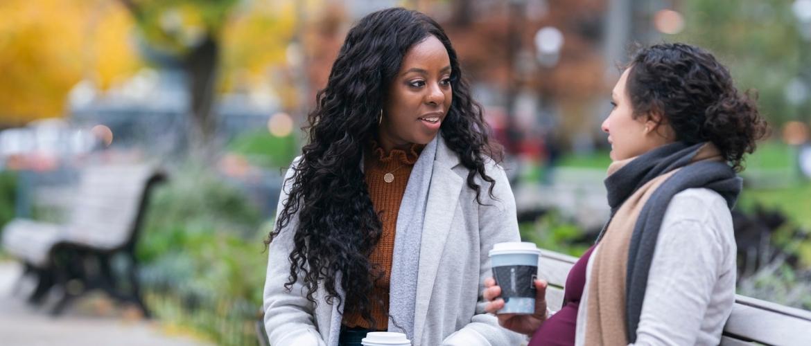 Two women talking and drinking coffee outside.