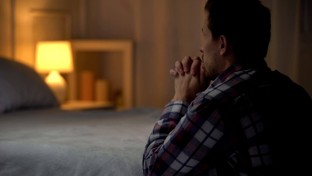 A man praying by his bed at night.