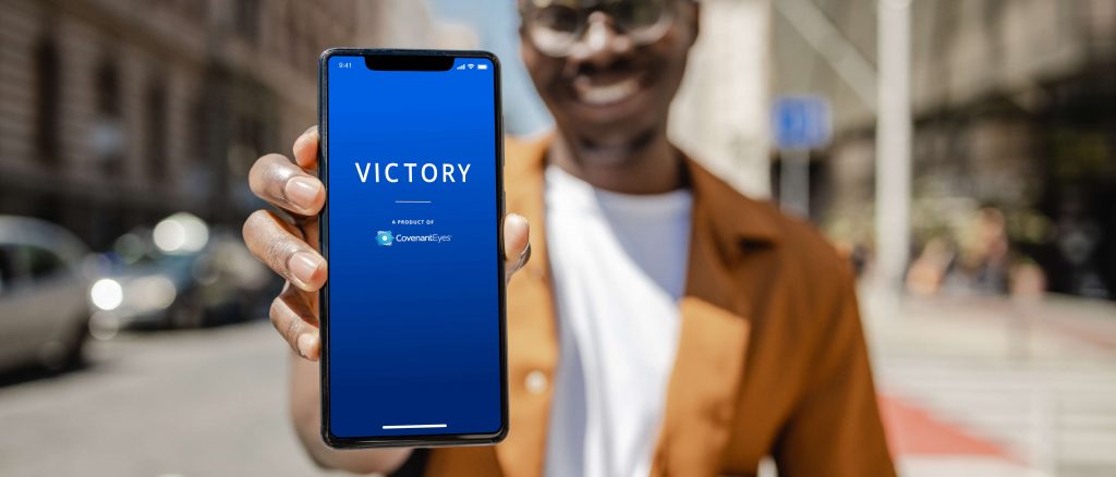 A man holding out a smart phone with "Victory" on the screen.