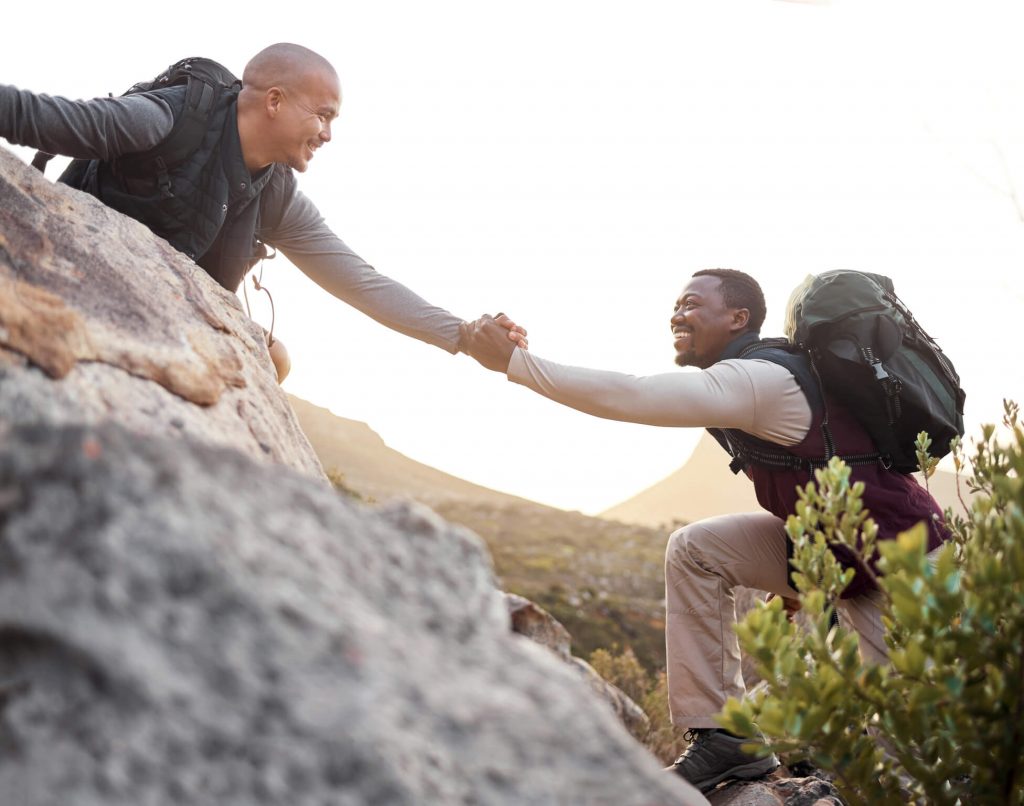 A man helping his friend hike a steep mountain.
