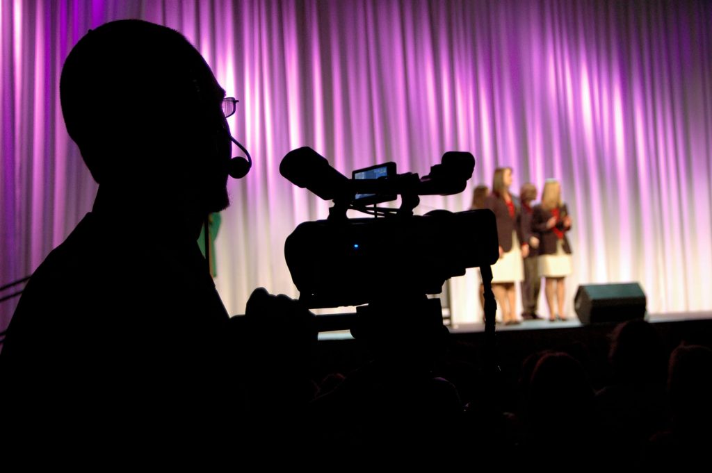 Camera man taping contestants on a stage.