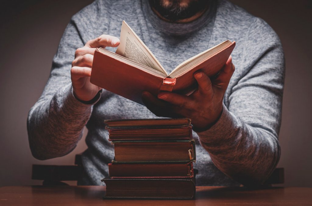A man reading a stack of old books.
