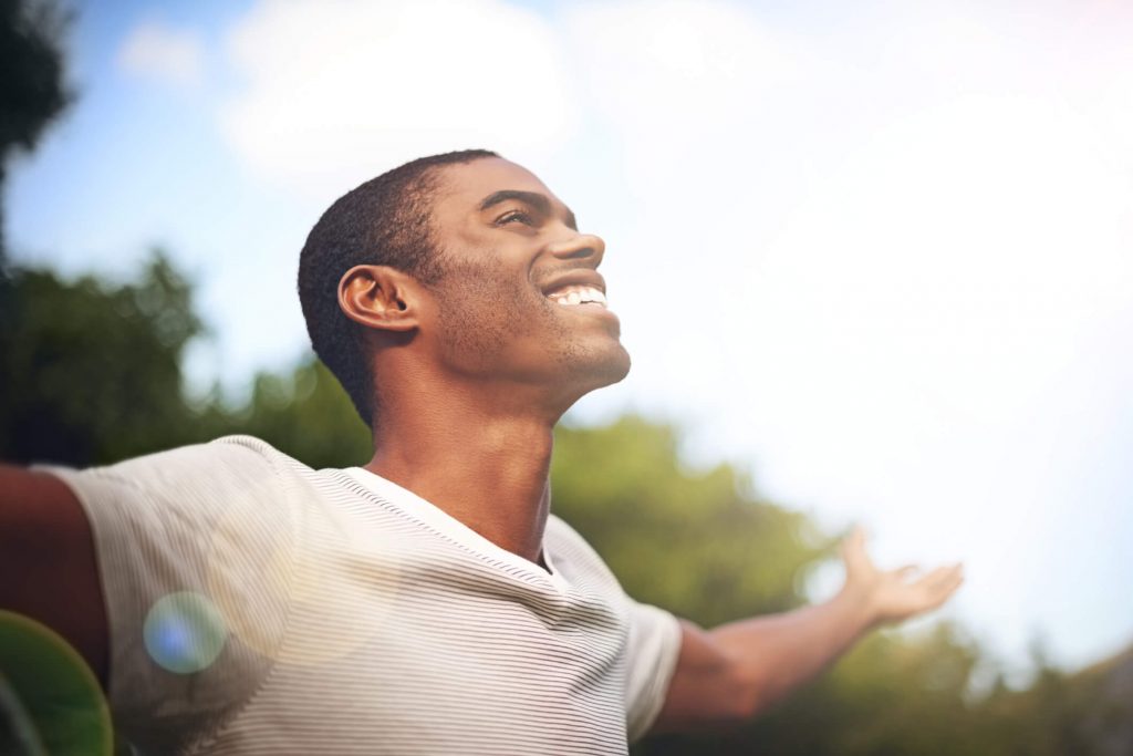 A young man with arms spread smiling in the sunshine.