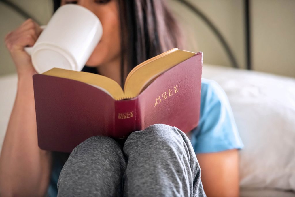 A woman doing her devotions and drinking coffee.