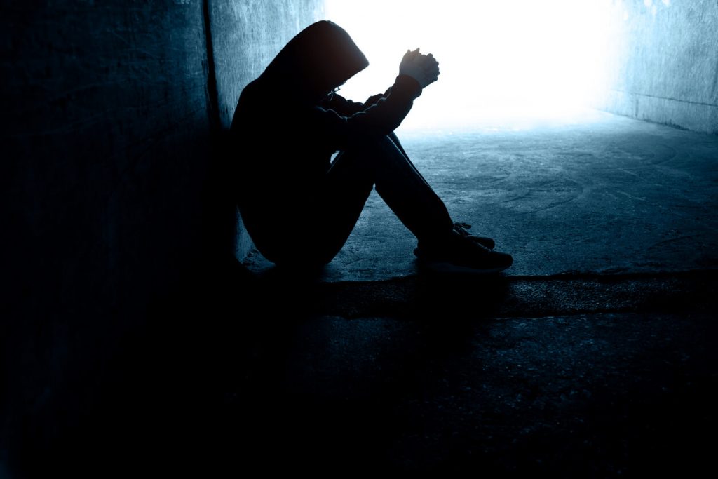 A man in a dark alley praying.