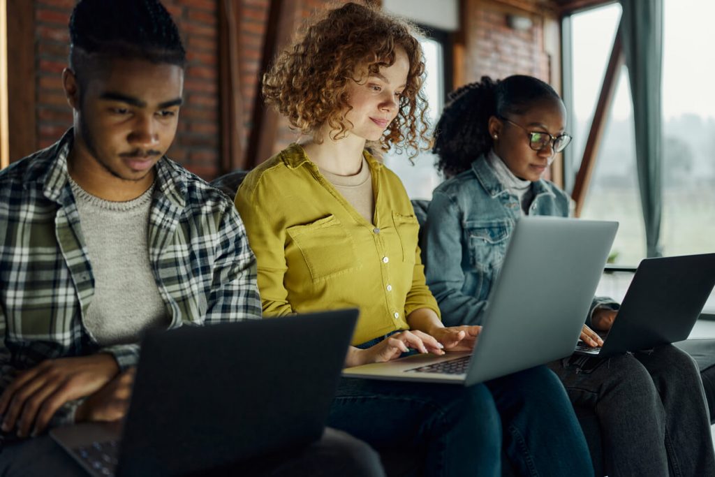 A group of three young computer programmers working on laptops.