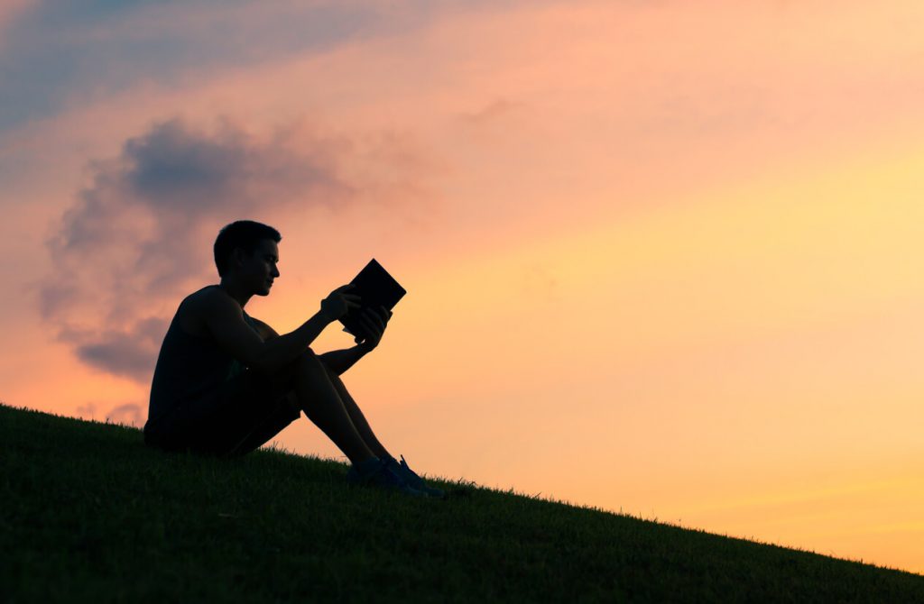 Silhouette of a young man outdoors reading Bible verses about masturbation.