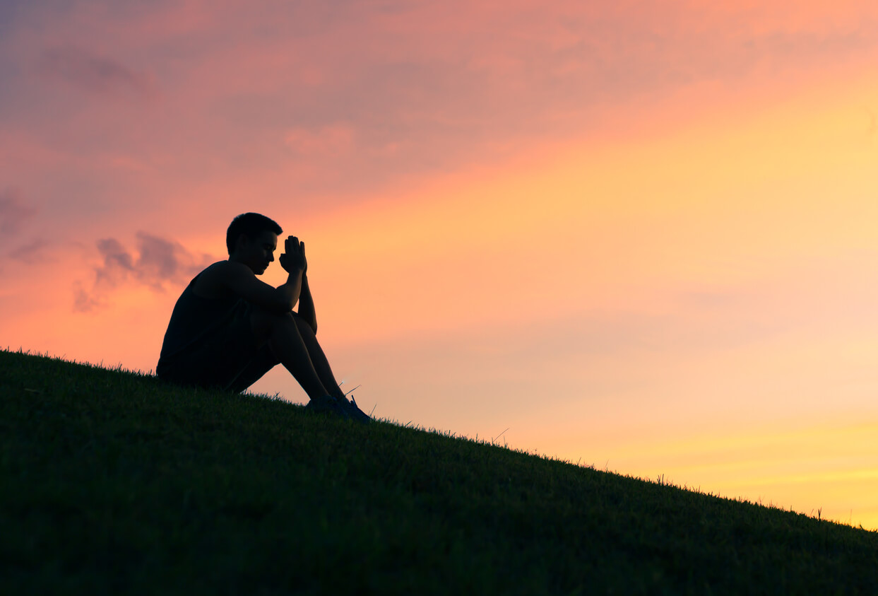 Silhouette of man praying on a hillside.