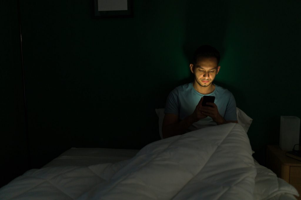 Man sitting in bed looking at his phone.