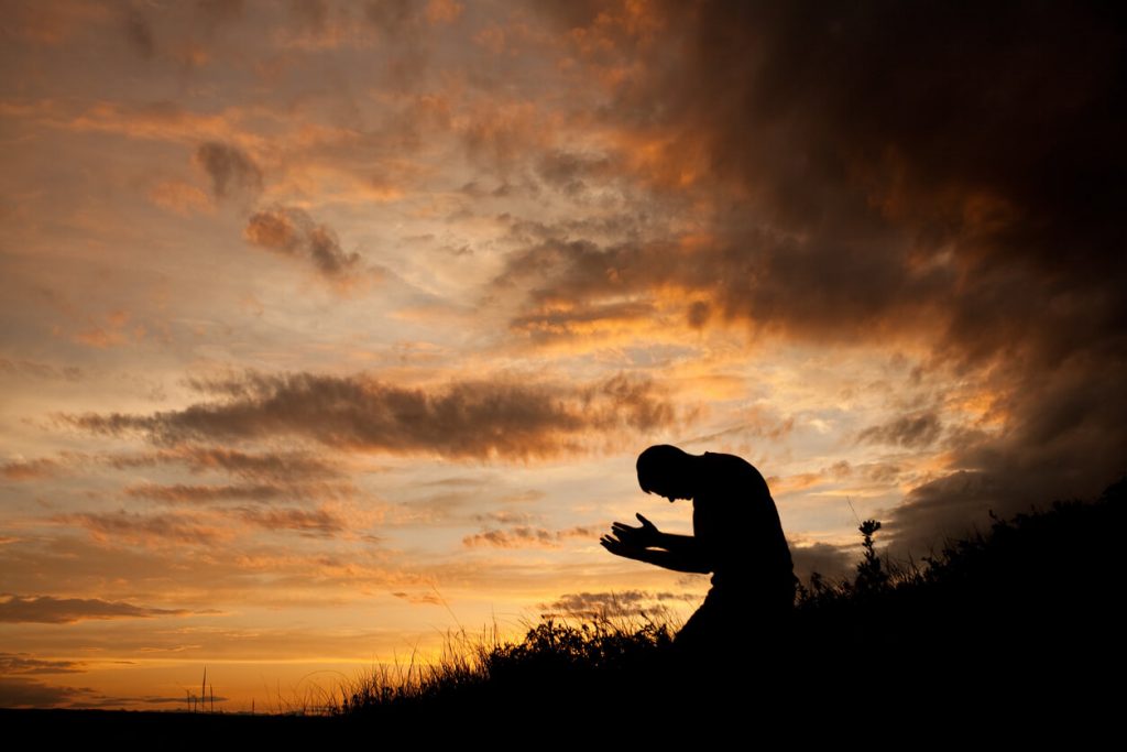 Silhouette of a man praying on a hillside.