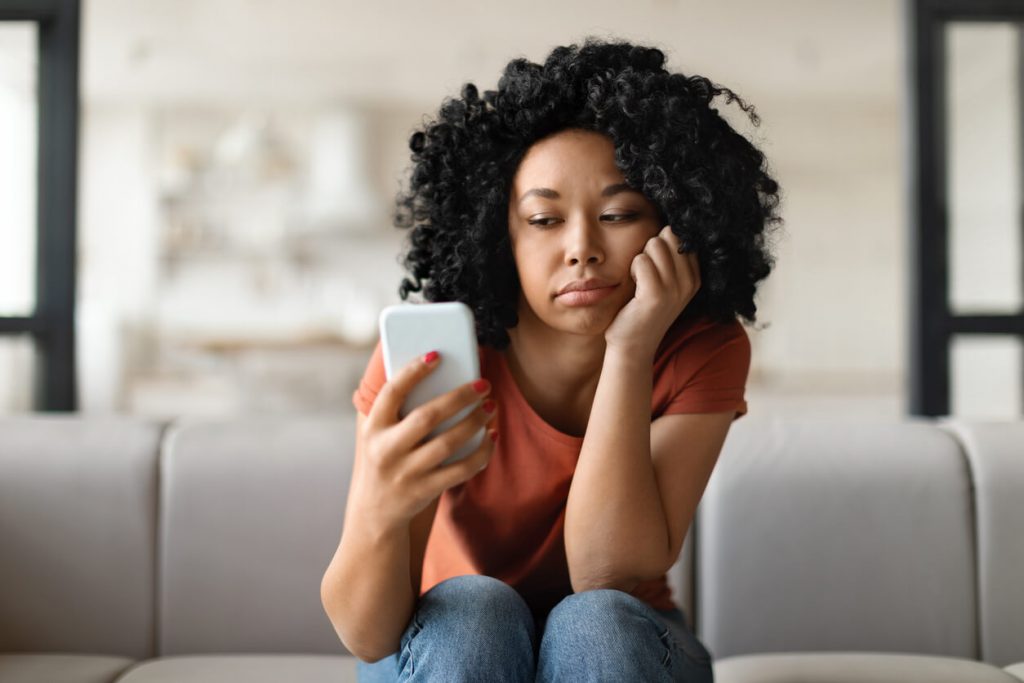 A woman looking at her smartphone with a confused expression.