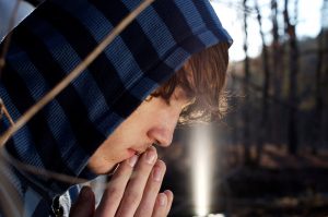 Young man wearing a hoodie praying.