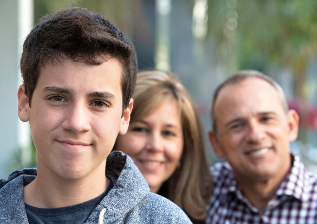 A smiling young man with his parents in the background.