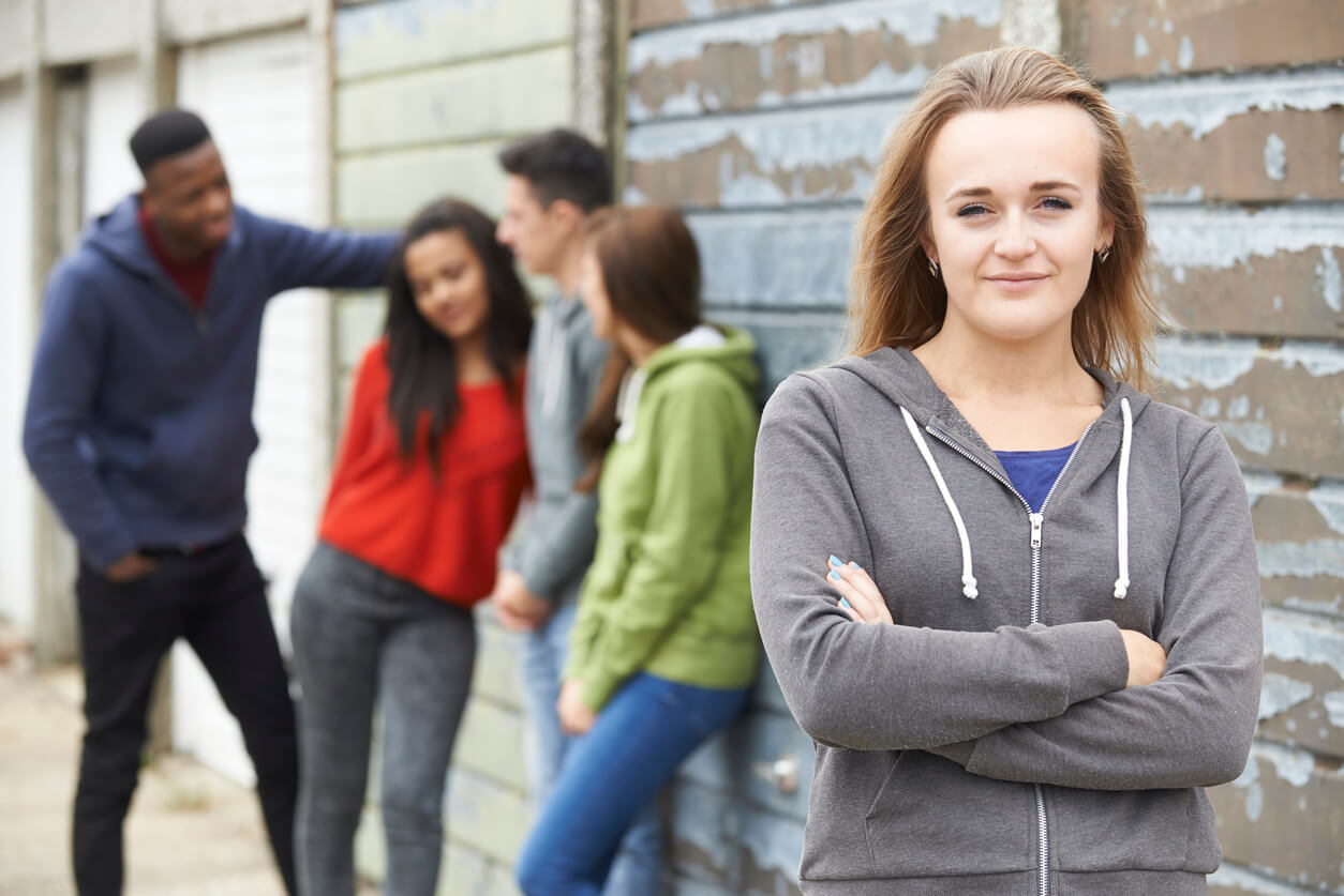 A teenage girl standing apart from a group of friends.