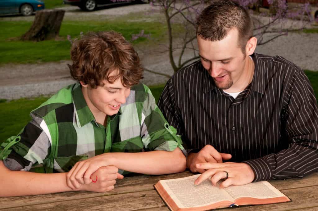 A father teaching the Bible to his teenage son.