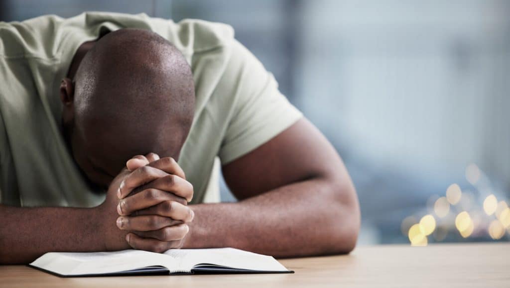A young man with bowed head praying over his Bible.