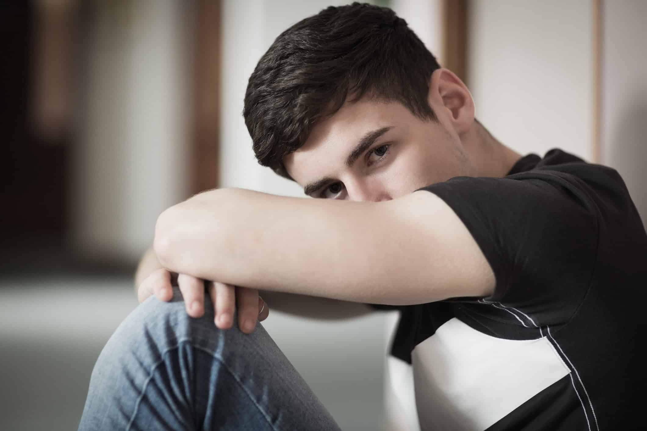 Close-up portrait of male student with head on knees sitting by wall in college