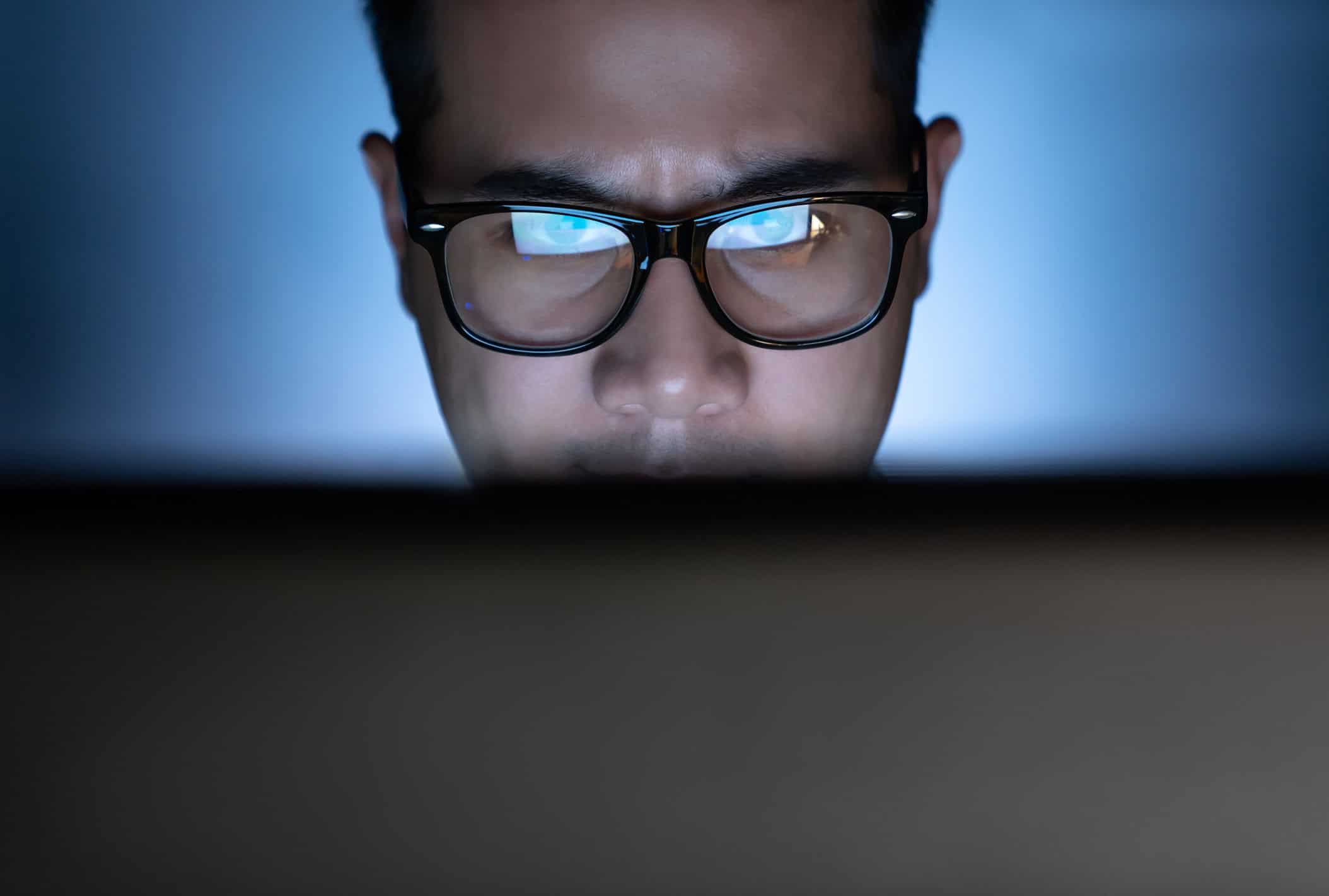 A man in a dark room looking at a bright computer screen.