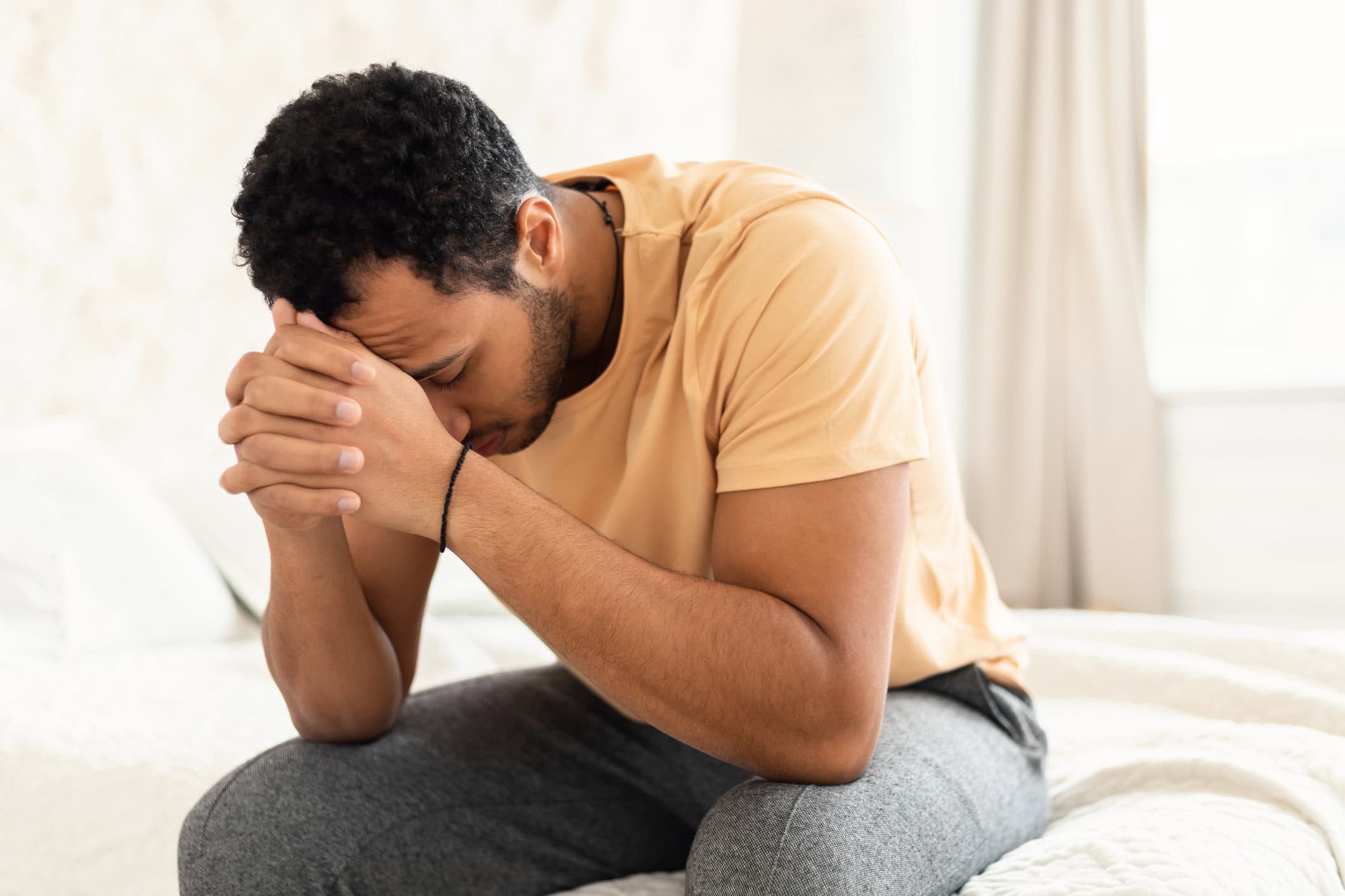 A young man sitting on his bed praying.