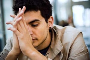 Young man with folded hands in front of his face