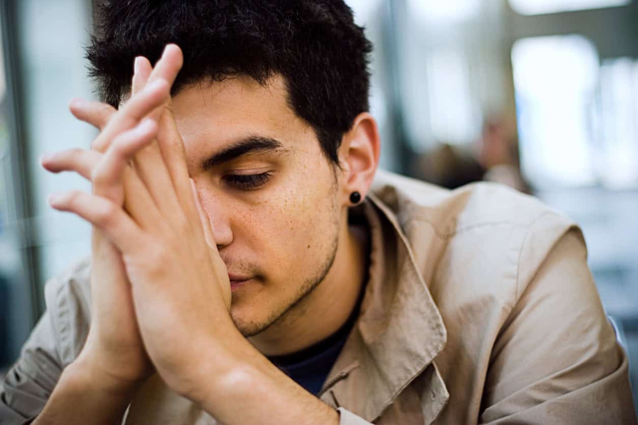 Young man with folded hands in front of his face