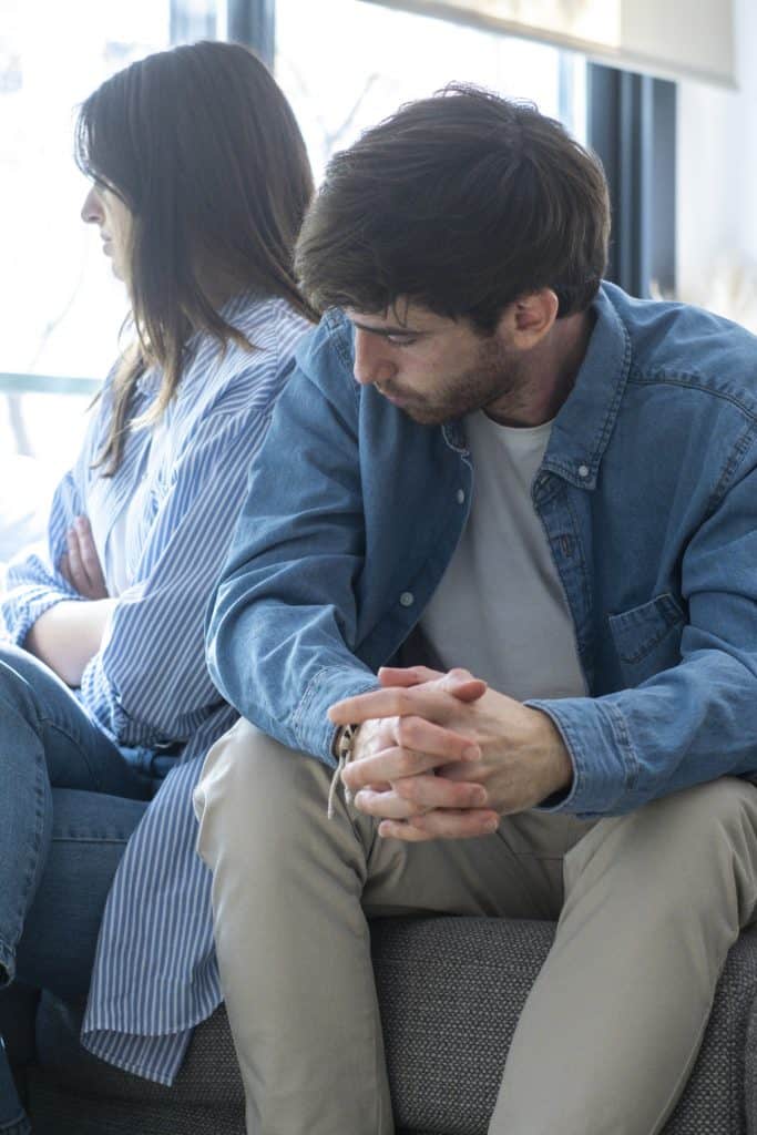 A husband and wife sit on the couch in a difficult conversation.