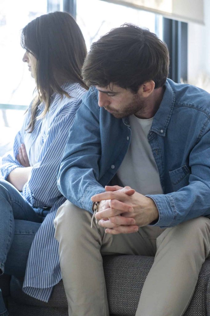 A husband and wife sit on the couch in a difficult conversation.