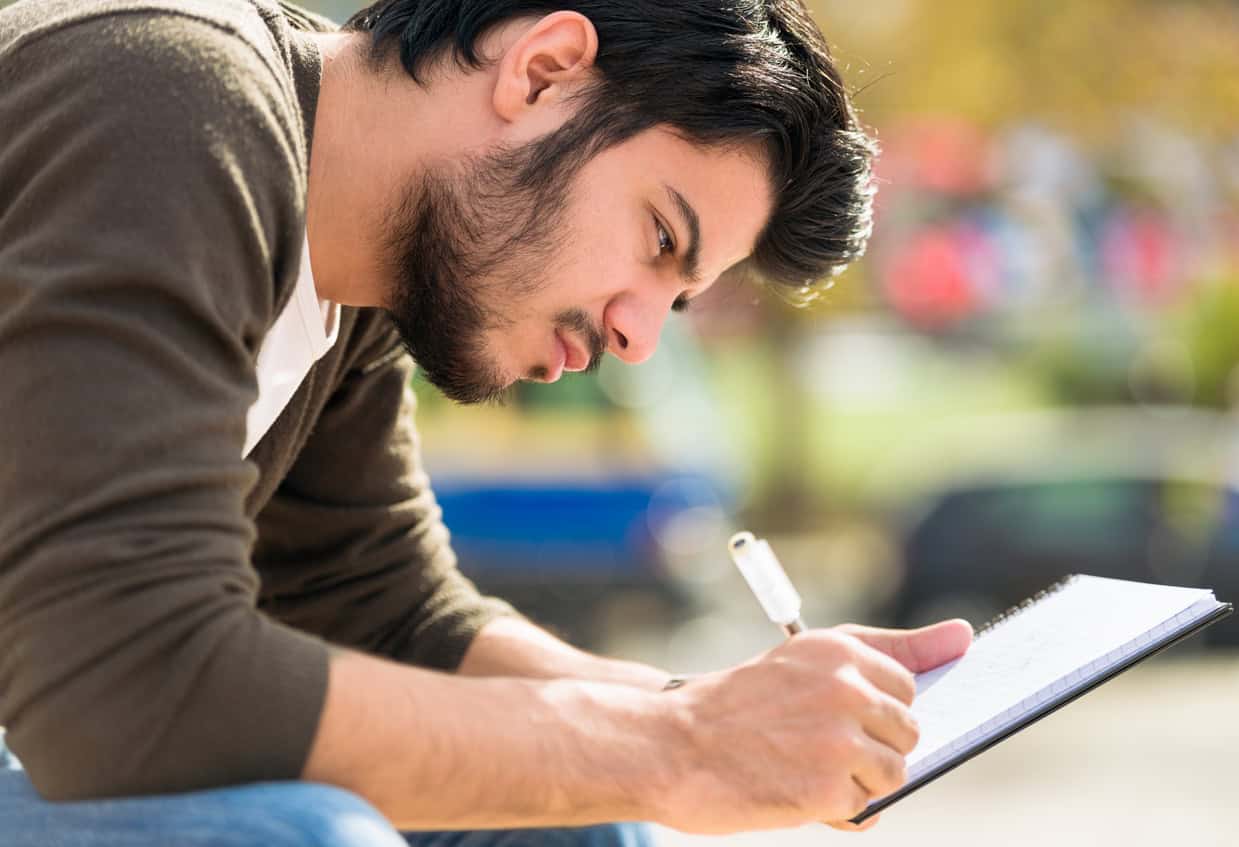 Close-up of a young man writing his journal outdoors