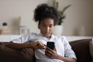 Young woman using smartphone, sitting on couch, confident young female looking at phone screen.