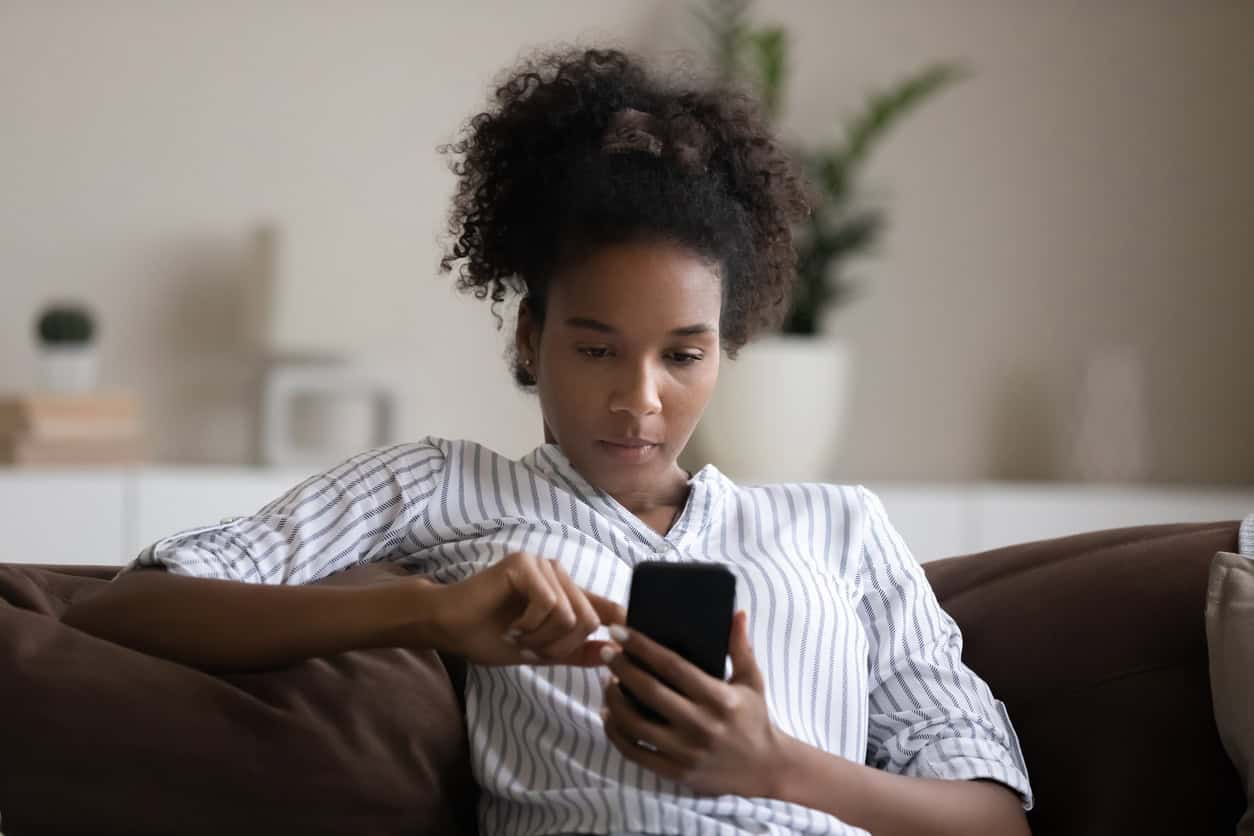Young woman using smartphone, sitting on couch, confident young female looking at phone screen.