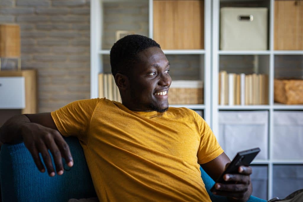 Young happy man using his smartphone while relaxing in sofa at home